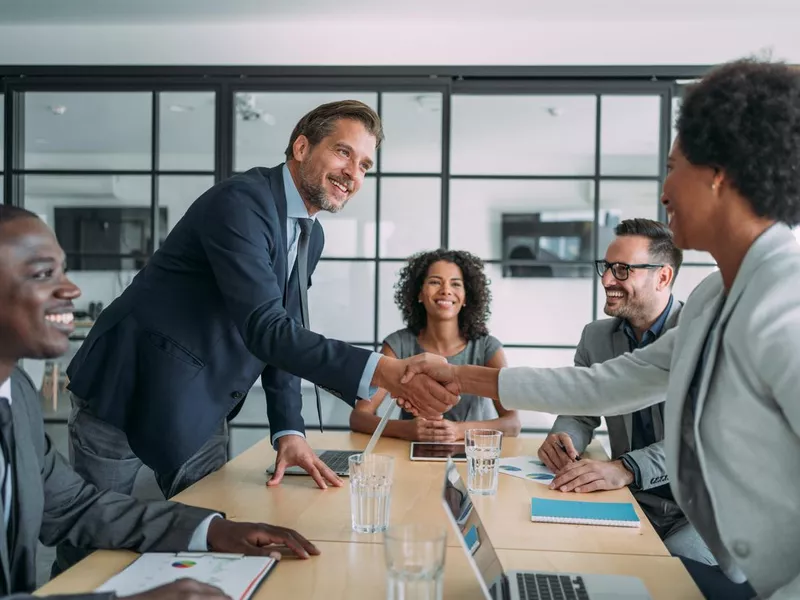 Businesswoman and businessman shaking hands across the table.